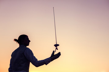 Silhouette of fencer man throwing up his fencing sword on a sunset background