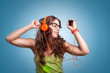 Beautiful girl with long curly hair in headphones and glasses with closed eyes listening to music and dancing. Portrait girl on blue background. Human facial expressions, emotions, feelings.