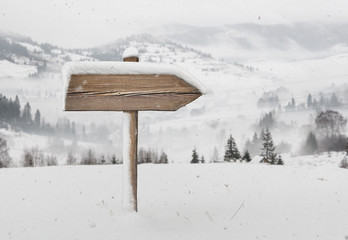 Wooden direction sign with less snow and mountains on background