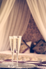 Two champagne glasses with oriental canopy bed at the background