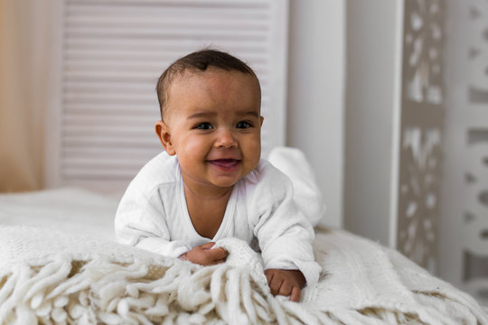 Cute mixed race African American baby boy plays inside on a bed