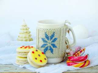 Sandwich biscuits with yellow icing sprinkled with sugar stars and cup of tea on light wooden background.  Christmas and New Year cookies