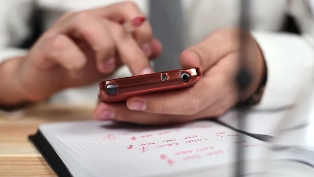Businessman Using His Cellphone And Taking Notes In Notepad. Close Up