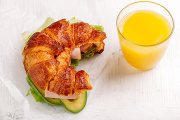 French fresh baked croissant sandwich with ham avocado, lettuce for breakfast on white workplace Office lunch Top view