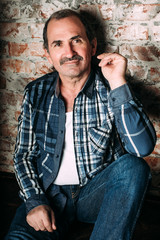 Obraz premium Handsome middle aged man is dressed in a casual clothing. Red brick wall background.