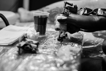 Tattoo master in black gloves, tattoo on the skin of black ink tattoo of his client in the salon.