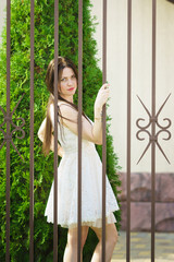 Beautiful girl in a white dress standing by the lattice fence