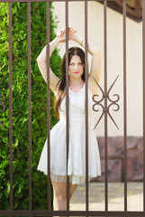 Beautiful sad girl in a white dress standing by the lattice fence
