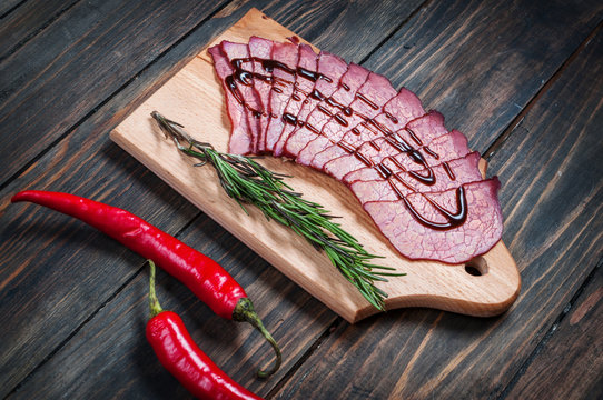 Sliced ham, chilli pepper, rosemary on a wooden board