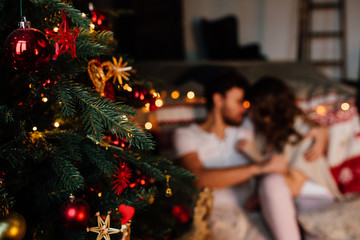 Couple in in pajamas resting on the floor next to the bed near the Christmas tree.