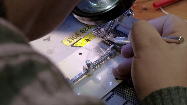 White man repairing broken smartphone iphone in workshop. Preparing motherboard to replace chip