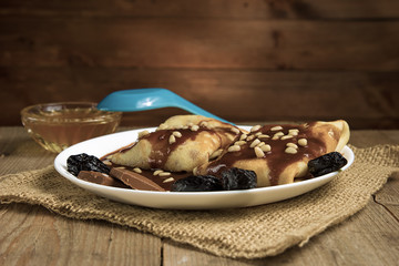 Pancakes with berries, fruits, chocolate, pine nuts and honey on white plate on a natural wooden board