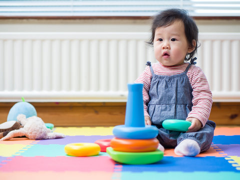 Adorable baby girl sitting on play mat and playing toy at home
