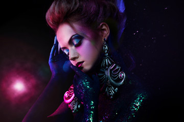 Young attractive blonde girl in bright art-makeup, in purple tones. Rhinestones and glitter body painting.