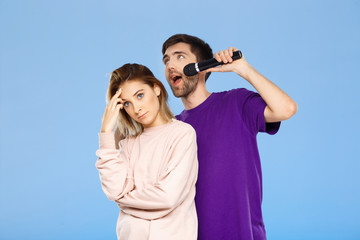 Beautiful couple over blue background. Man singing in microphone girl didpleased.