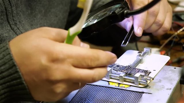 White man repairing broken smartphone iphone in workshop. Change chip.