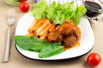 Dish of beef goulash with penne pasta, lettuce and spinach
