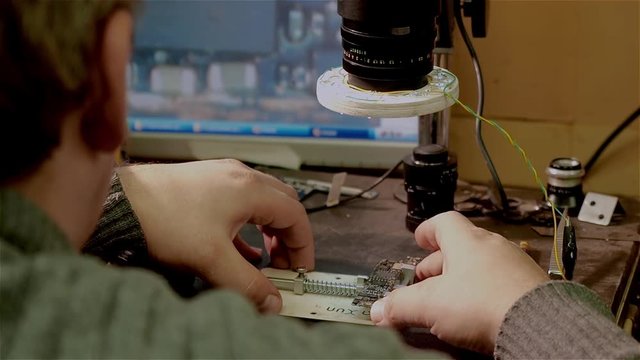 White man looks through handmade electronic microscope on repair of motherboard smartphone iphone
