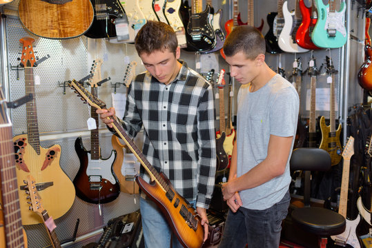 Two boys holding electric guitar in musical instrument shop