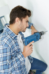 male builder drilling holes in wall at construction site