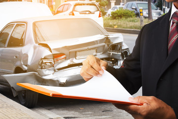 man writing on clipboard while insurance agent examining car after accident