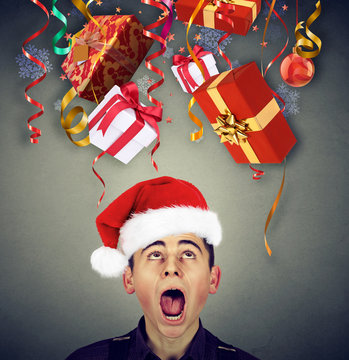 Surprised man in santa claus hat looking up at multiple christmas gifts