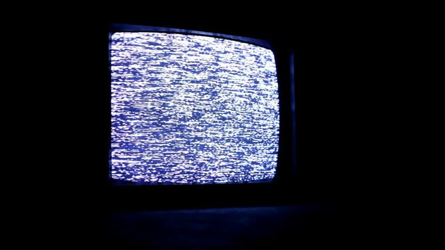 Old vintage television playing blank static screen in dark.