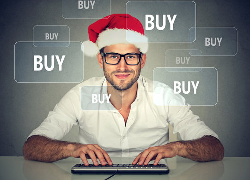 Happy christmas man in red santa claus hat buying stuff online