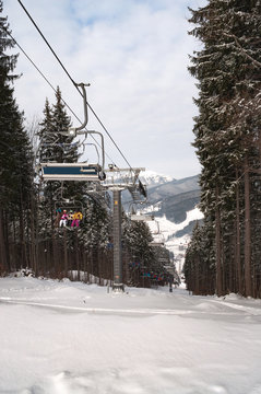 Happy skiers and snowboarders rising up on ski lift in the mountain winter resort