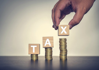Tax concept wooden blocks and coins on table with a hand hold a type X.