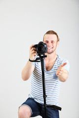 Handsome photographer with camera on monopod, on gray background