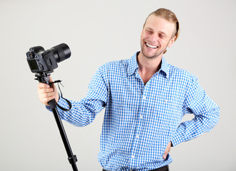 Handsome photographer with camera on monopod, on gray background