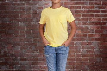 Young African American boy in blank yellow t-shirt standing against brick wall