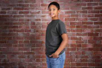 Fototapeta na wymiar Young African American boy in blank gray t-shirt standing against brick wall