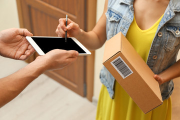 Young woman appending signature after receiving parcel from courier at home, closeup