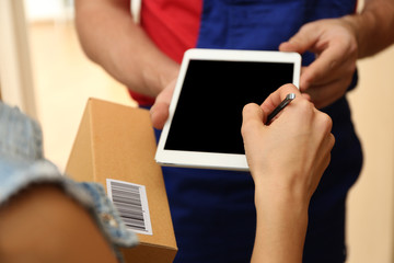 Young woman appending signature after receiving parcel from courier at home, closeup