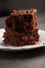 Walnut brownie cake stacked on white plate on dark wooden background macro shot