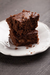 Fototapeta na wymiar Walnut brownie cake stacked on white plate on dark wooden background slightly above shot