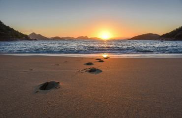 Beautiful sunrise with the sun rising from the Atlantic Ocean, solar path on the water and footprints at the deserted Praia Vermelha Beach, Rio de Janeiro, Brazil