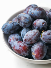 Fresh plums in a bowl on white background