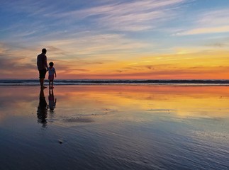 Silhouette of father and child at beach shoreline during sunset