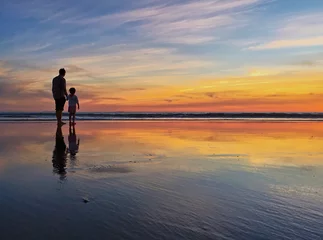 Fototapeten Silhouette of father and child at beach shoreline during sunset © samantoniophoto