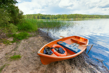 Lifebuoy in bright orange boat standing on the shore of a picturesque lake in the summer