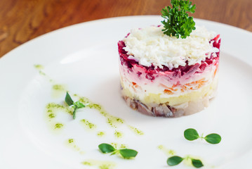layered salad with herring, beets, carrots, onions, potatoes and eggs close-up on a plate