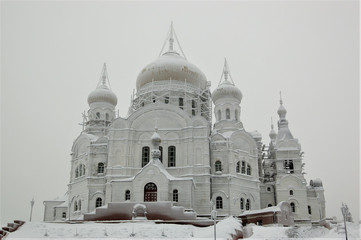 Obraz premium Белого́рский Свято-Никола́евский православно-миссионе́рский мужско́й монасты́рь. Крестовоздвиженский собор в снежном инее на высокой горе и заснеженная дорога к нему. Зима