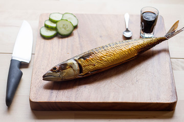 Top angle of a mackerel grilled lying on chopping board with slice cucumber and soy sauce and spoon...