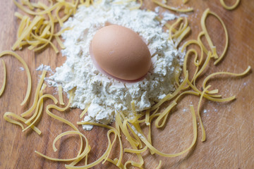 An egg on top of white flour with Chinese noodles on chopping board, a preparation for cooking,  Italian spaghetti,mie, typical Chinese food