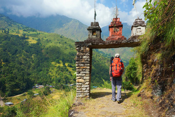 Tourist, a man, enter the gate to nepalese village at the valley on Annapurna Circuit Trek, in Annapurna Himal, Himalaya, Nepal, Asia