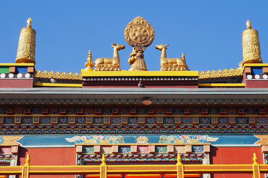 Upper part of the roof of a traditional Tibetan Buddhist temple. Architectural details, the deers, the wheel of samsara, prayer wheels, bright patterns, colorful decoration. Kathmandu, Nepal.