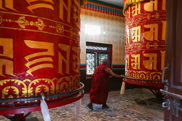Old bouddhist monk, a tibetan man, spins a huge prayer wheels at the Shechen monastery, Kathmandu,...